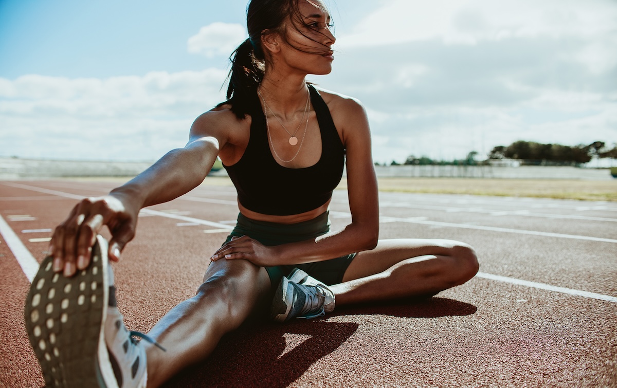 Athlete doing stretching exercises on running track. Woman runner stretching leg muscles by touching his shoes and looking away.