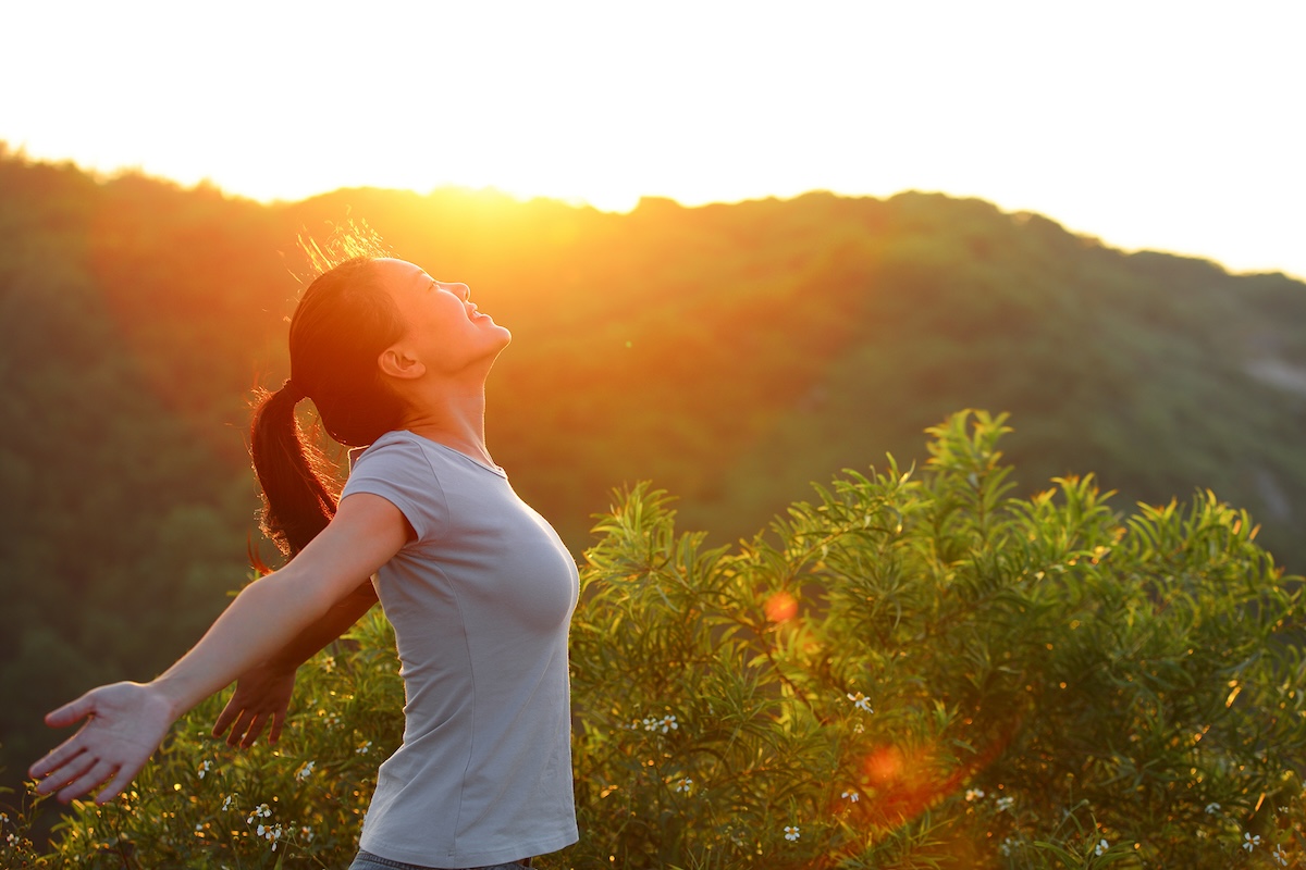 Freedom woman open arms at sunrise mountain peak wellness concept